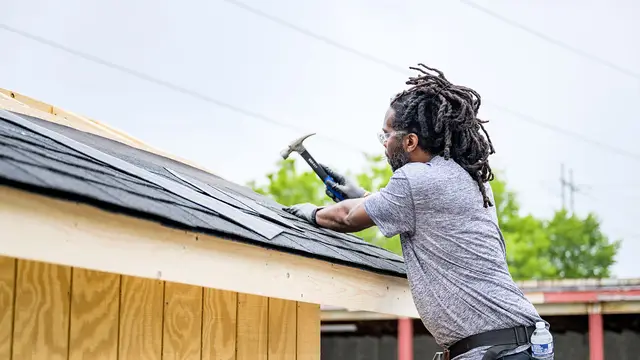 Roofer nailing shingles on a house roof